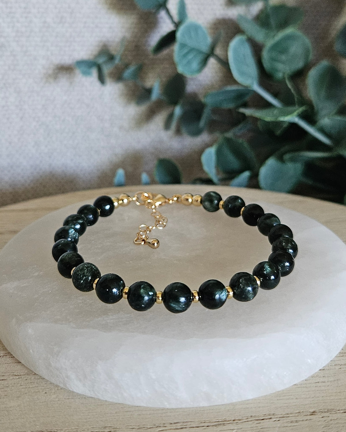 Seraphinite Echo bracelet with 6mm deep green gemstone beads, 14k gold-plated accents, lobster clasp and extender chain displayed on selenite