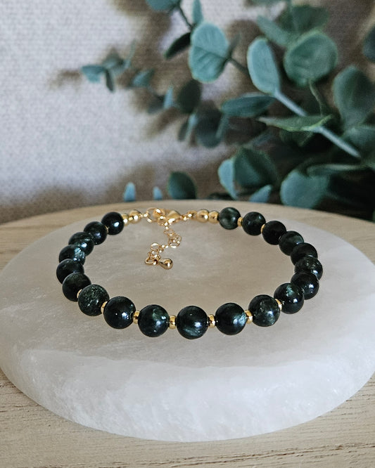 Seraphinite Echo bracelet with 6mm deep green gemstone beads, 14k gold-plated accents, lobster clasp and extender chain displayed on selenite
