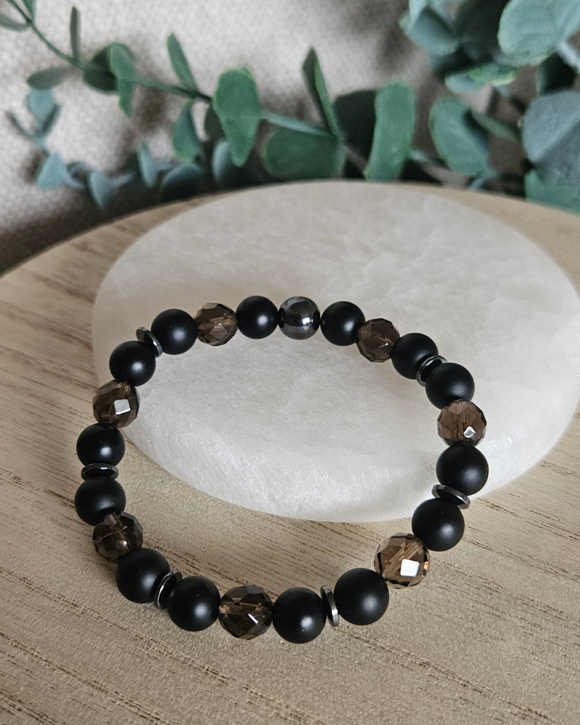 Smoky Quartz, Black Onyx and Hematite bracelet displayed on light wood beside a round selenite plate