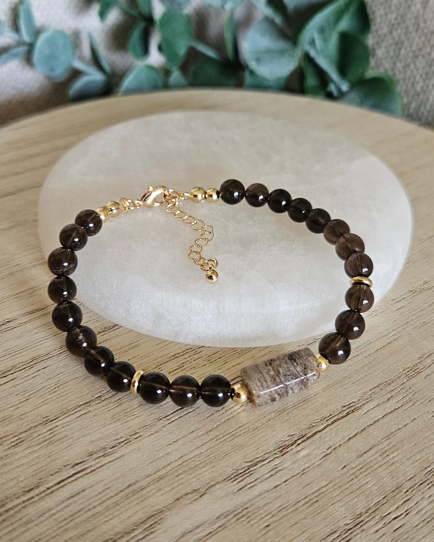 Smoky Quartz and Angel Phantom Quartz bracelet arranged before a selenite plate with eucalyptus in the background