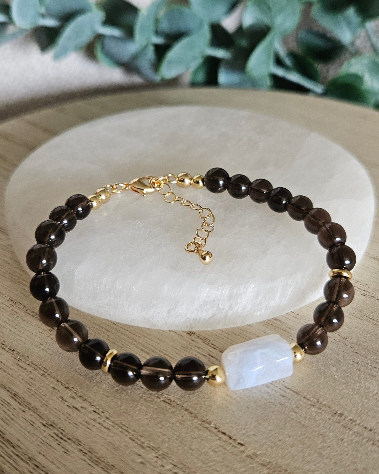 Smoky Quartz and Blue Lace Agate bracelet arranged before a round selenite plate with eucalyptus in the background
