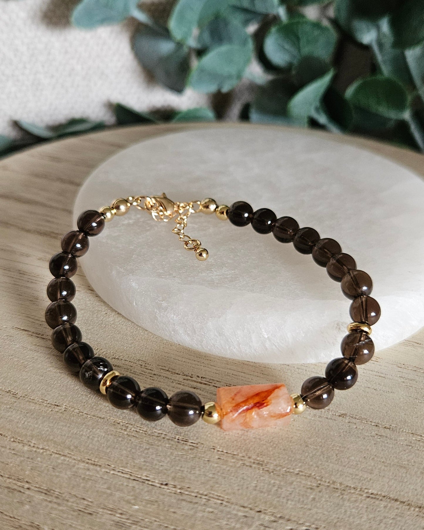 Smoky Quartz and Red Hematoid Quartz bracelet arranged before a selenite plate with eucalyptus in the background
