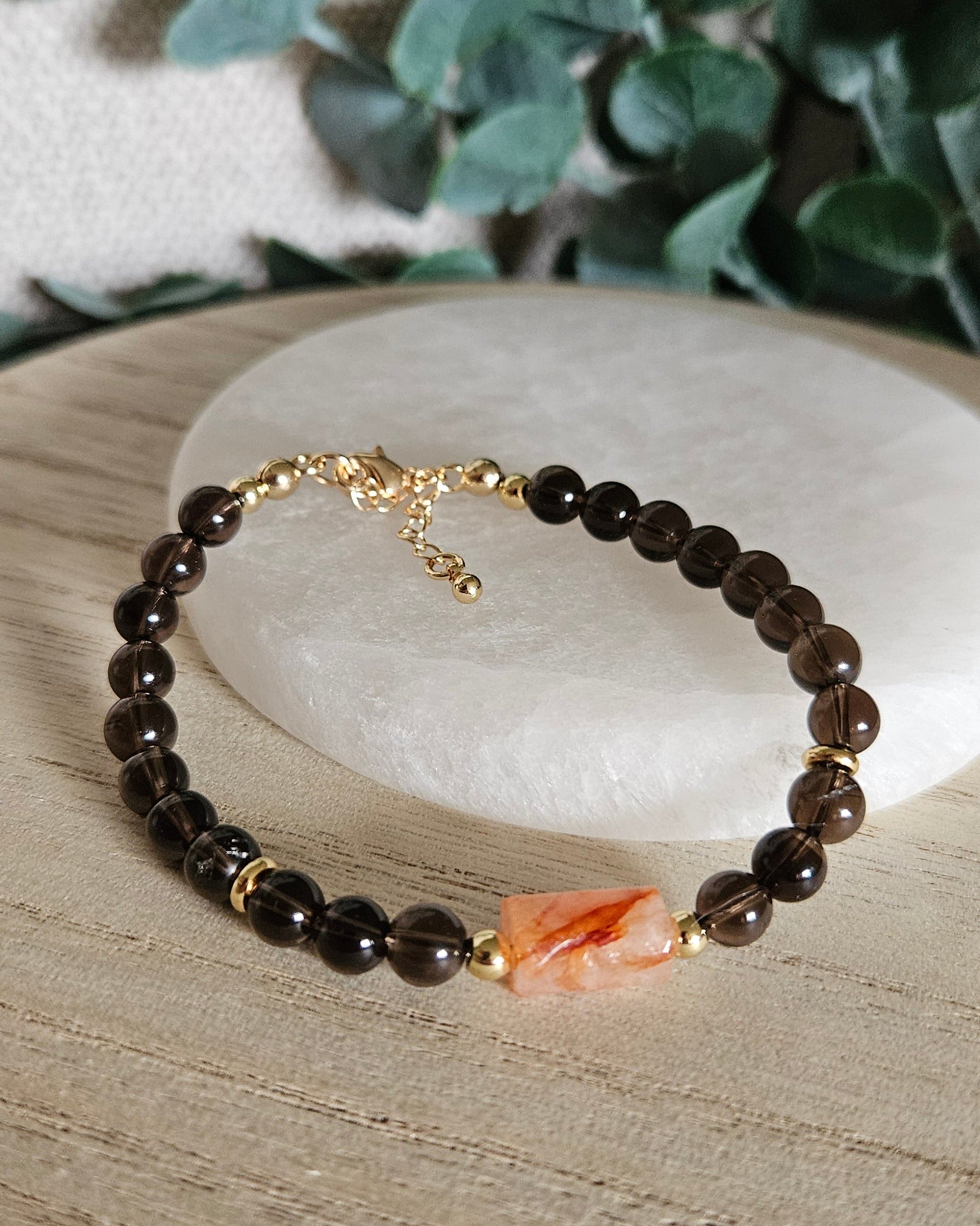 Smoky Quartz and Red Hematoid Quartz bracelet arranged before a selenite plate with eucalyptus in the background