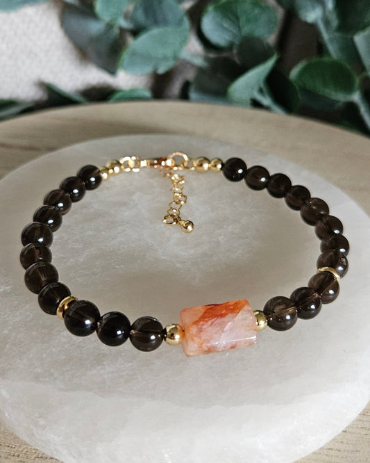 Smoky Quartz bracelet with a Red Hematoid Quartz focal, gold-plated accents and extender chain displayed on selenite