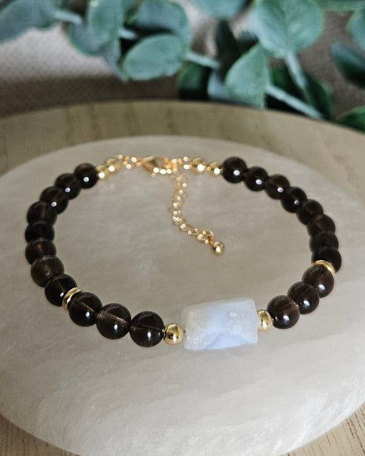 Smoky Quartz bracelet with a pale Blue Lace Agate focal, gold-plated accents and extender chain displayed on selenite