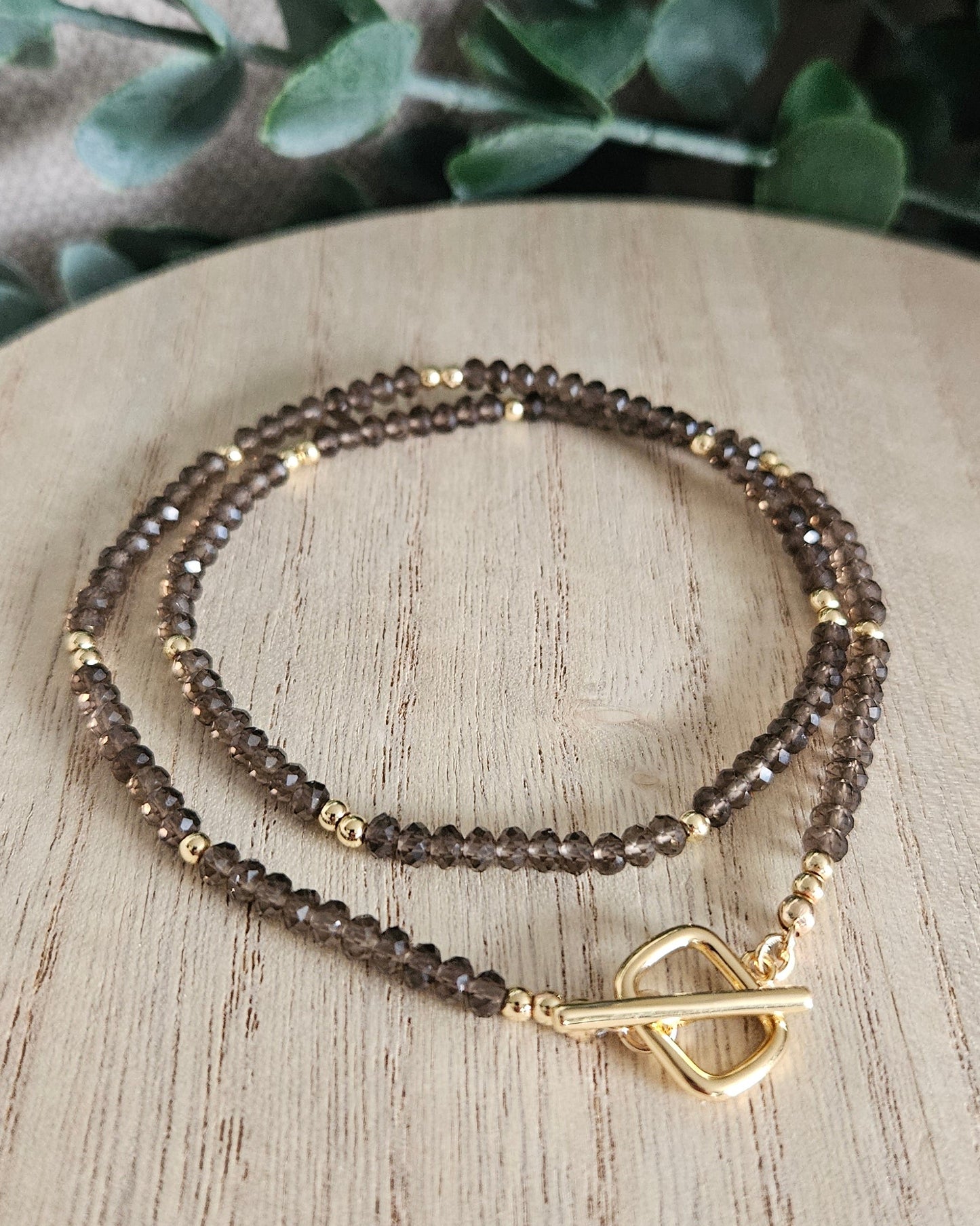 Smoky Quartz necklace loosely coiled on a wooden display with its gold-plated toggle clasp in front