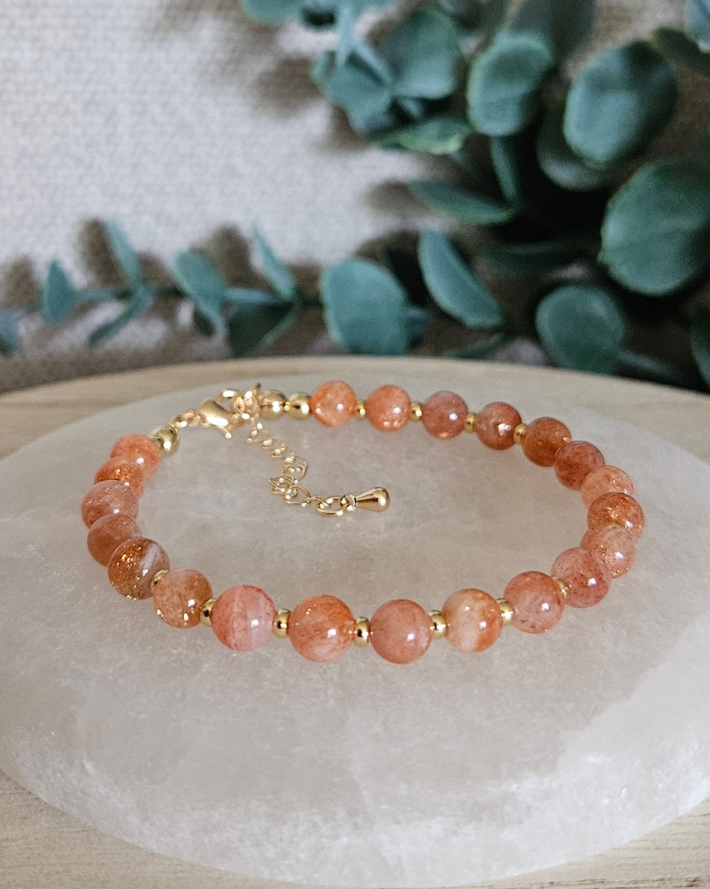 Sunstone Echo bracelet with gold-plated accents and clasp displayed on a round selenite plate