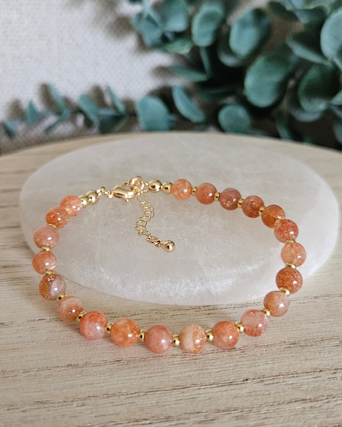 Sunstone Echo bracelet arranged before a selenite plate with eucalyptus in the background