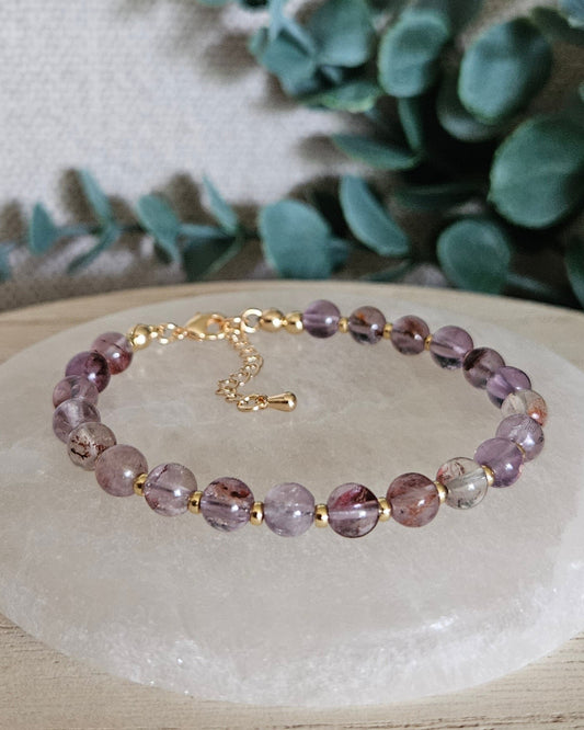 Super Seven Echo bracelet with gold-plated accents and clasp displayed on a round selenite plate