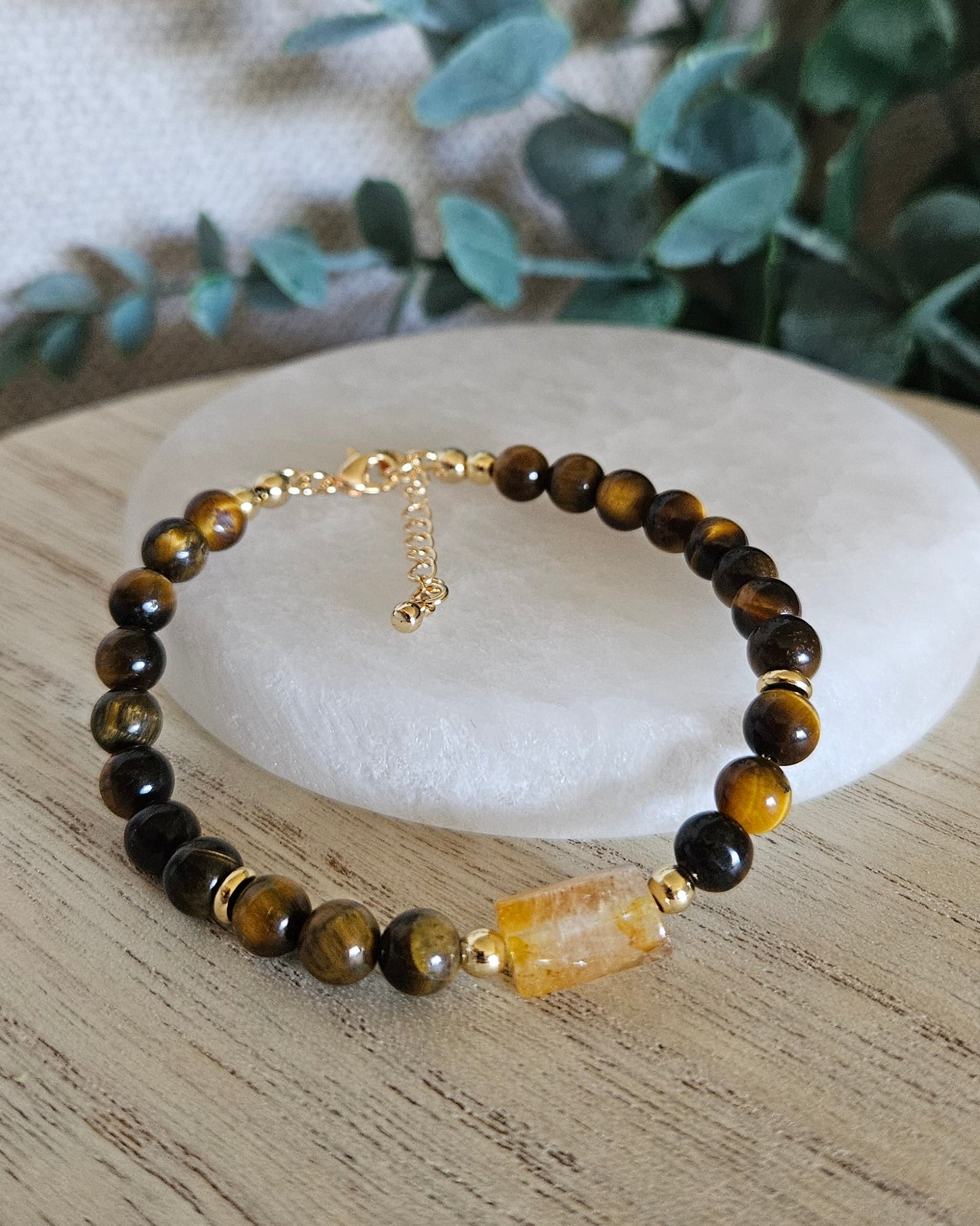 Tiger’s Eye and Citrine bracelet arranged before a round selenite plate with eucalyptus in the background