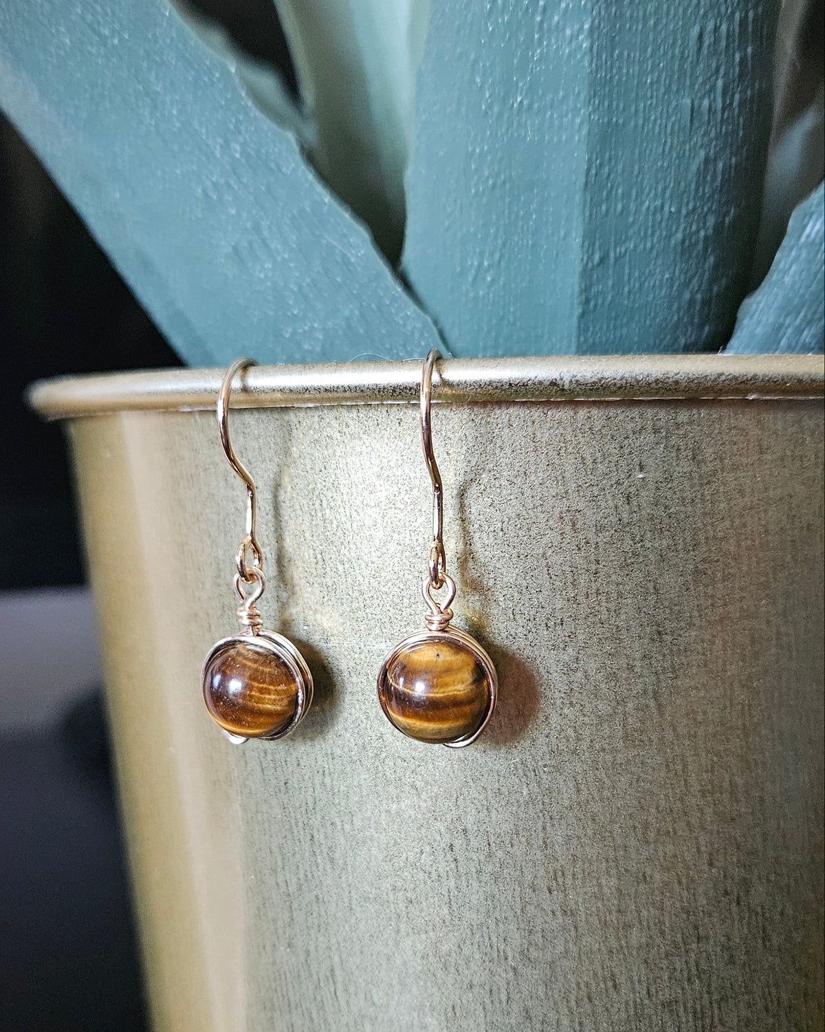 Tiger’s Eye wire wrapped earrings hanging on a gold plant pot with warm neutral styling