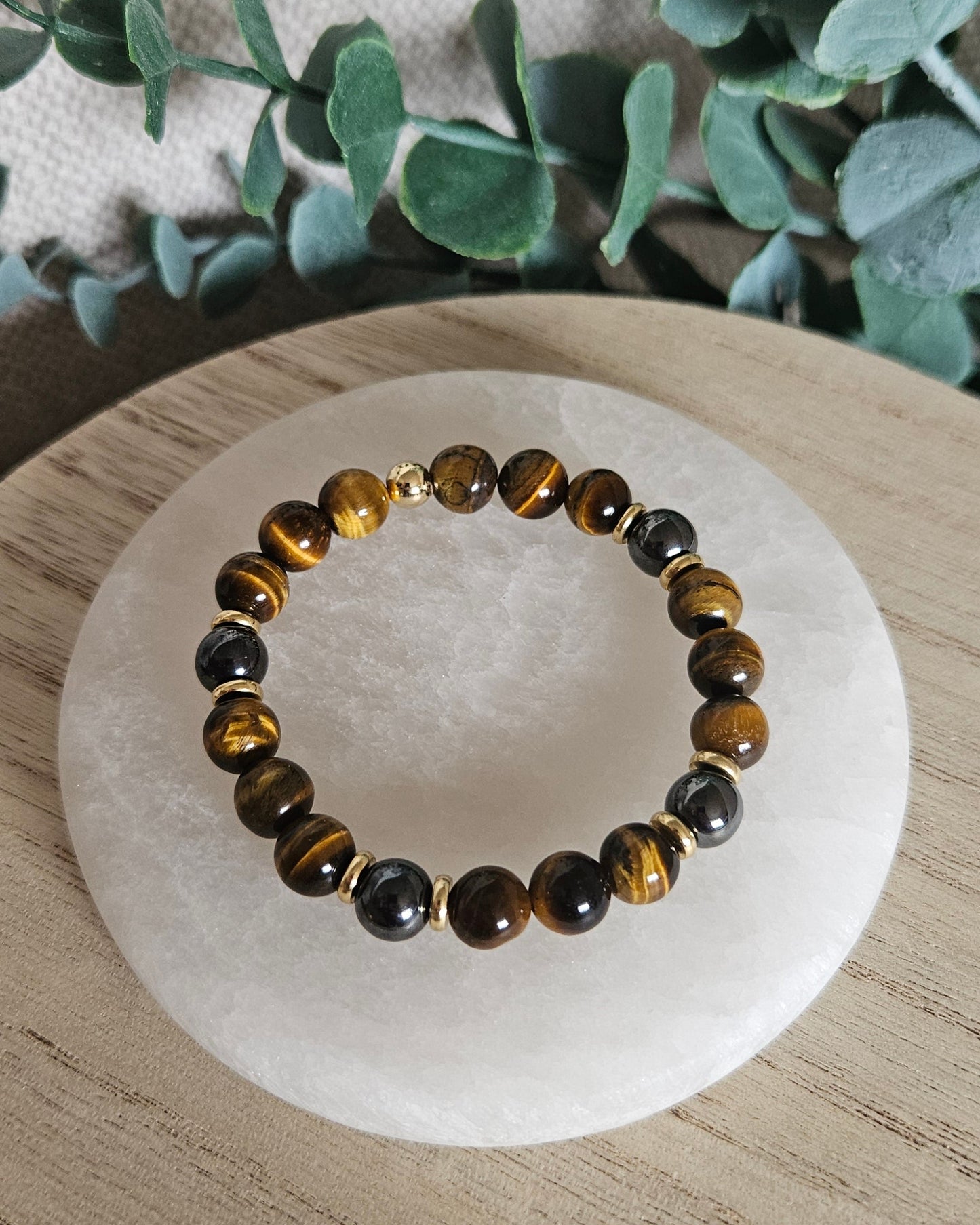 Close-up of golden-brown Tiger’s Eye and dark Hematite beads with gold-plated accents on a pale stone tray