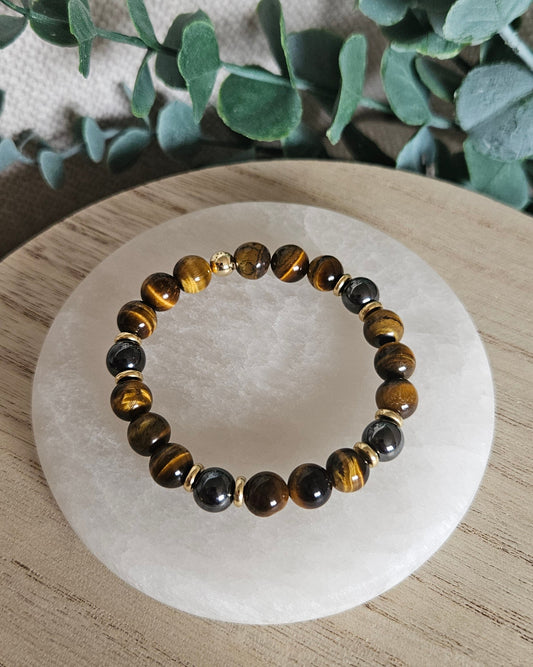 Close-up of golden-brown Tiger’s Eye and dark Hematite beads with gold-plated accents on a pale stone tray