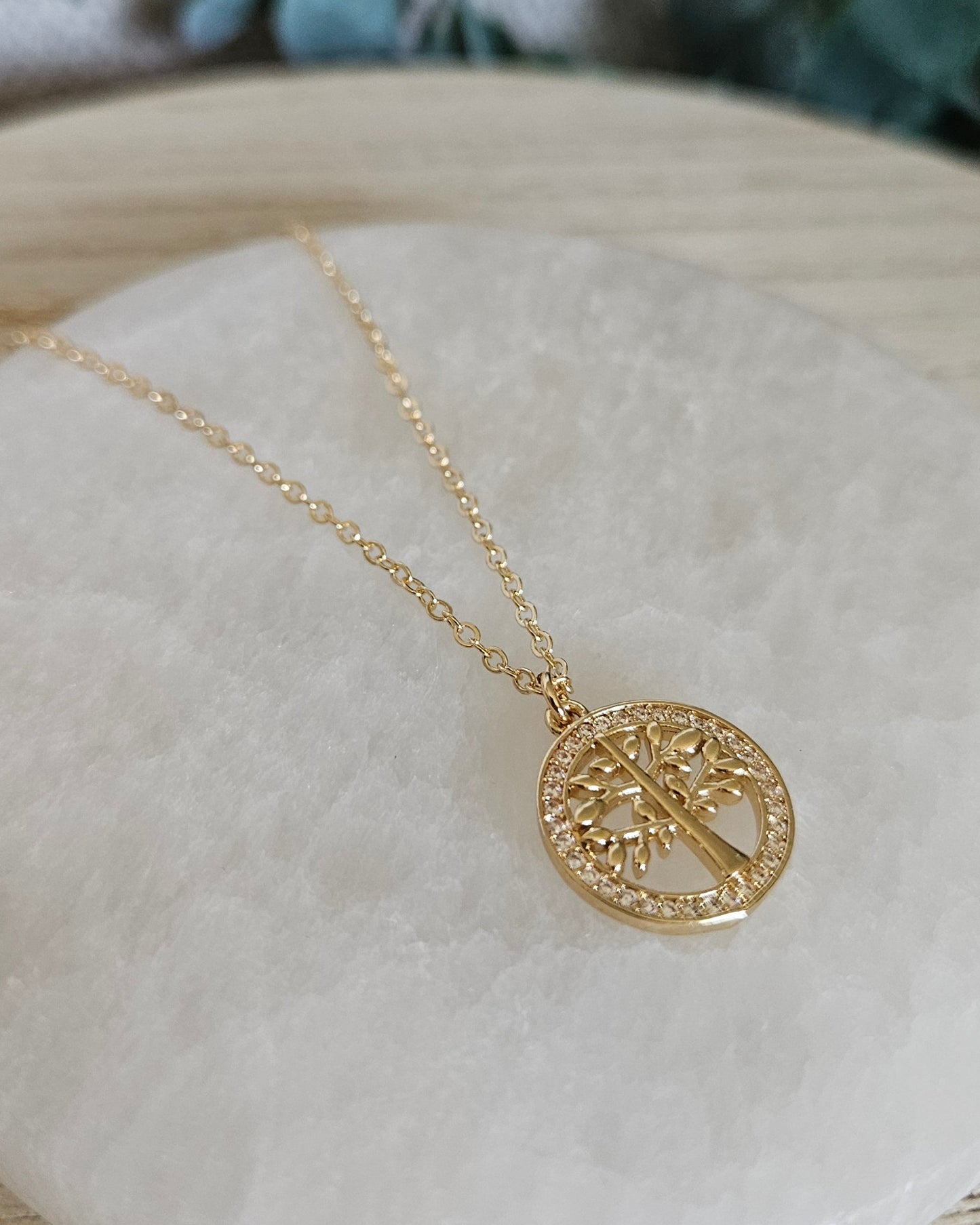 Angled view of the Tree of Life pendant and delicate gold-filled chain resting on a round selenite plate