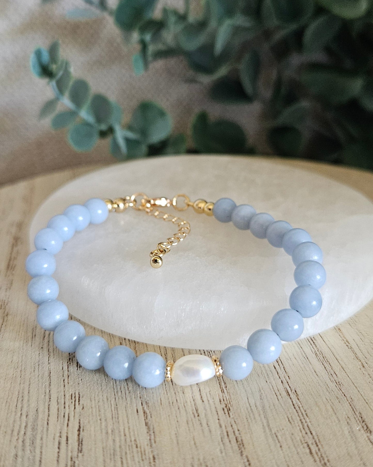 Angelite Embrace bracelet arranged before a selenite plate with a freshwater pearl focal and eucalyptus background