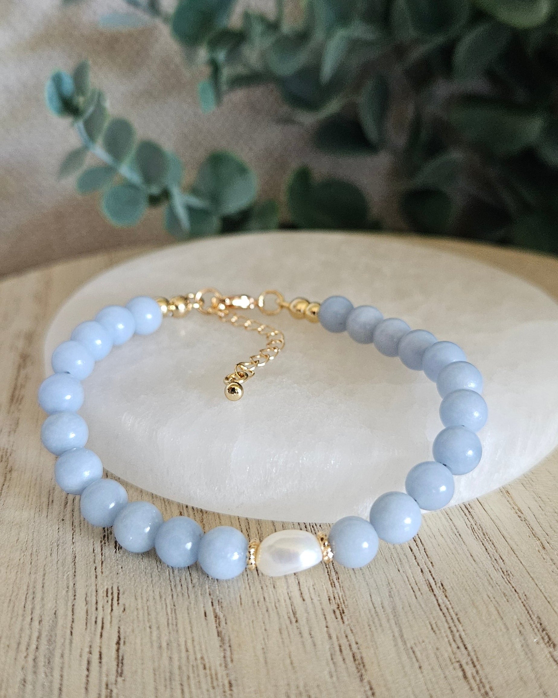 Angelite Embrace bracelet arranged before a selenite plate with a freshwater pearl focal and eucalyptus background