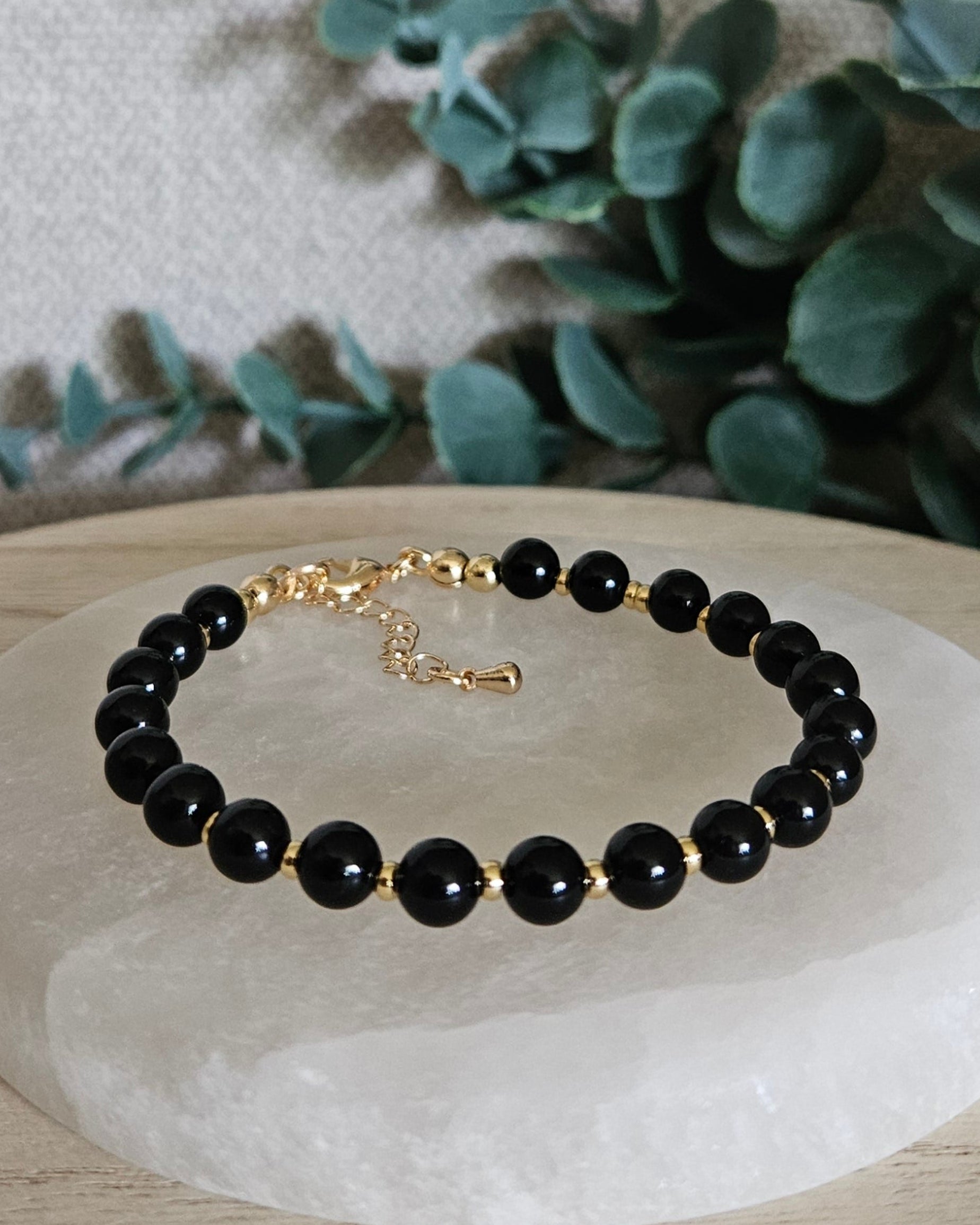 Black Onyx Echo bracelet with gold-plated accents and clasp displayed on a round selenite plate