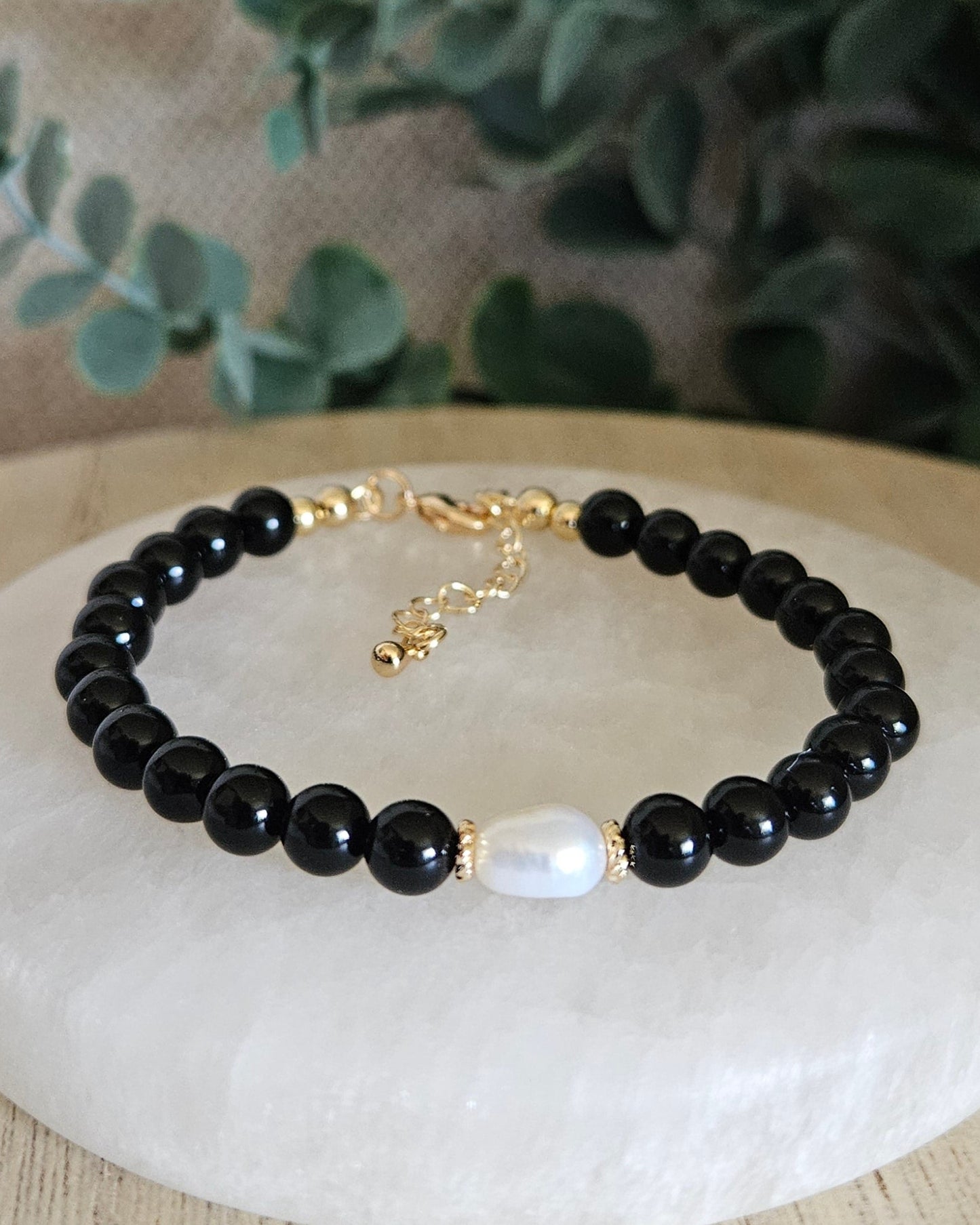 Black Onyx Embrace bracelet with freshwater pearl focal and gold-plated accents displayed on a selenite plate