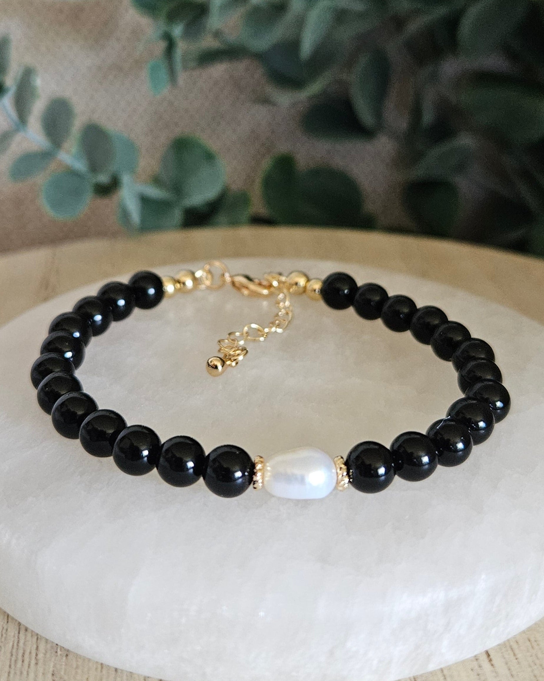 Black Onyx Embrace bracelet with freshwater pearl focal and gold-plated accents displayed on a selenite plate