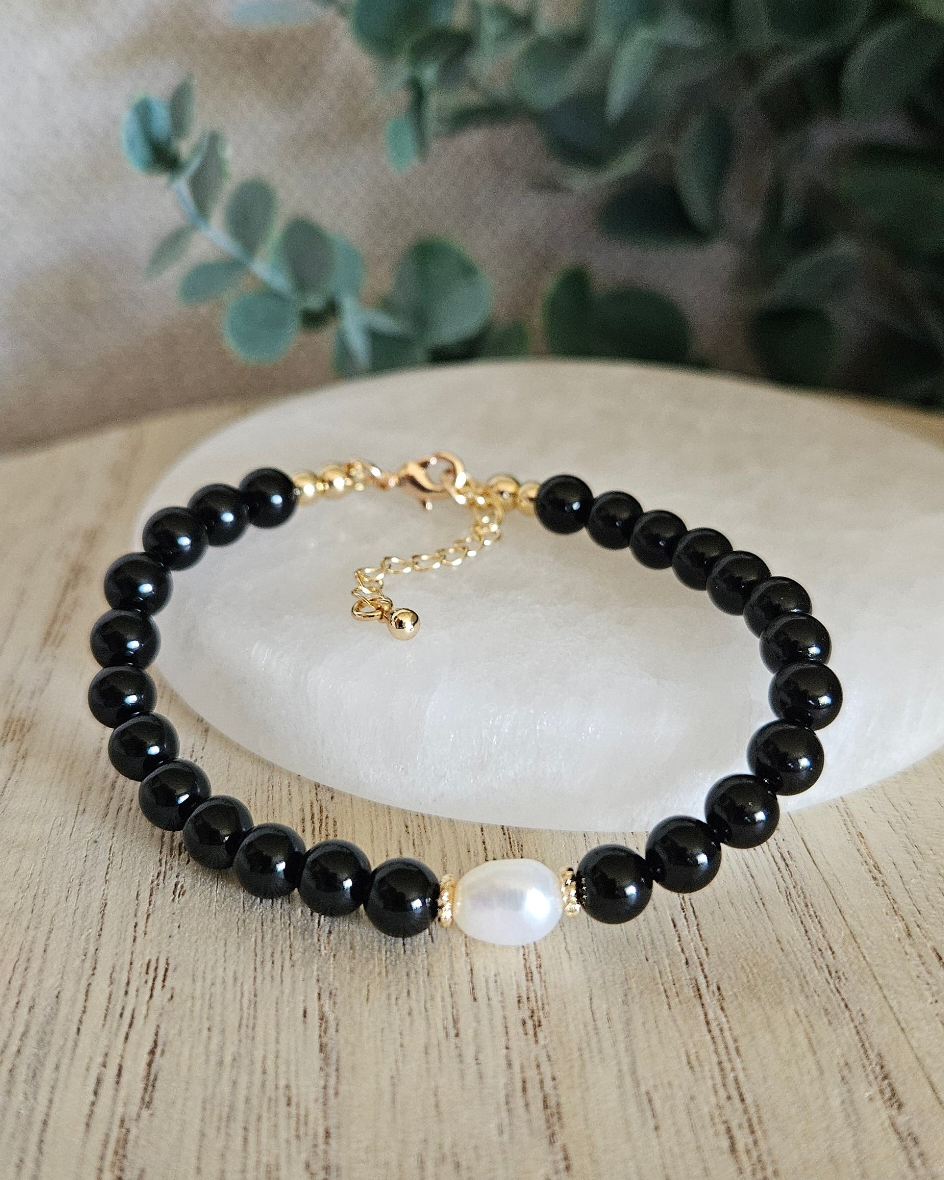 Black Onyx Embrace bracelet arranged before a selenite plate with a freshwater pearl focal and eucalyptus background