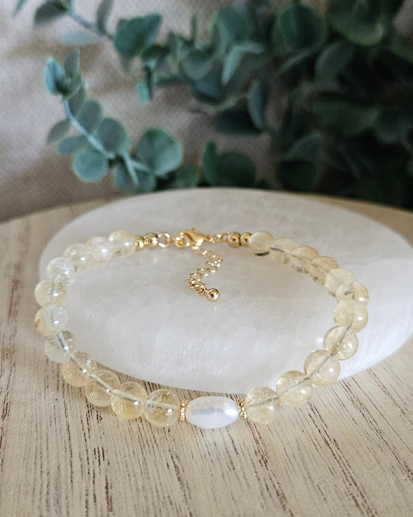 Citrine Embrace bracelet arranged before a selenite plate with a freshwater pearl focal and eucalyptus background