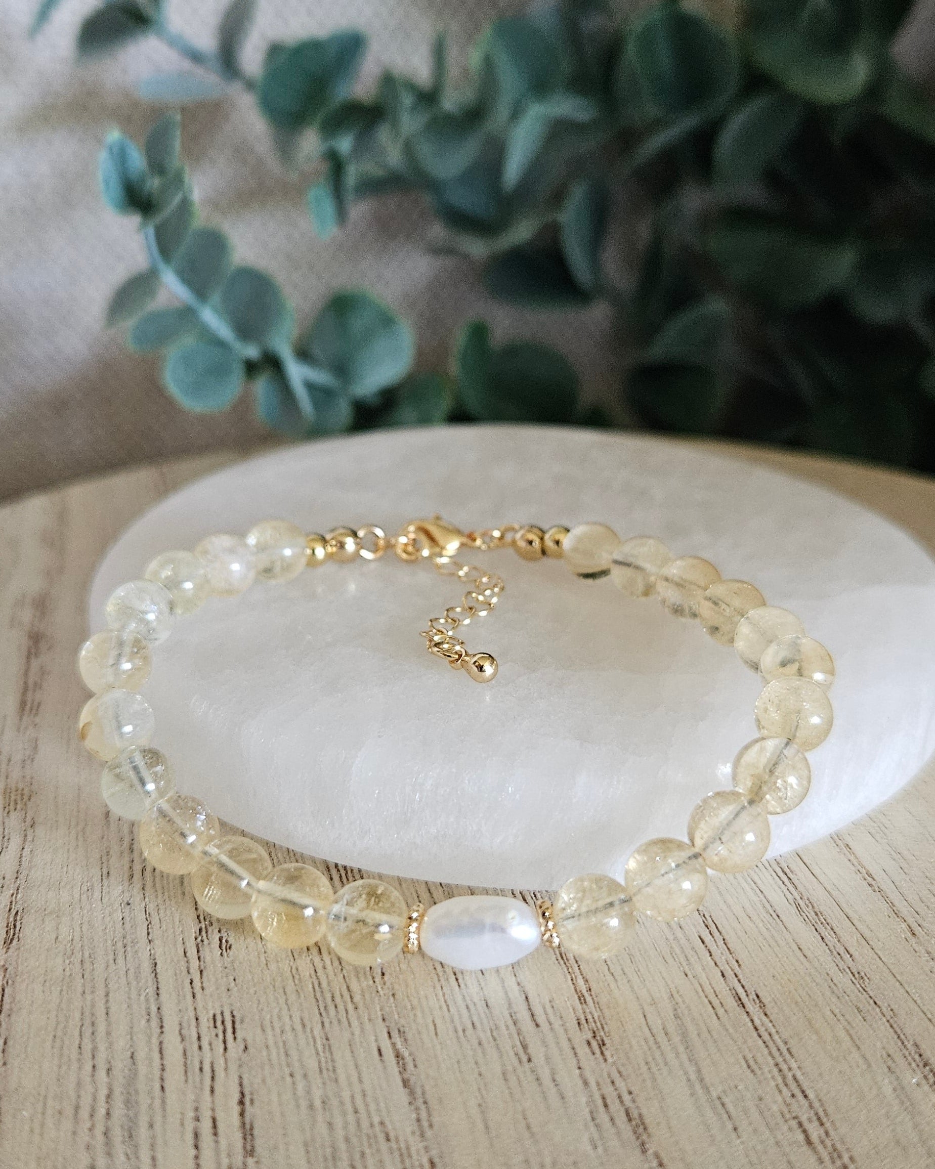 Citrine Embrace bracelet arranged before a selenite plate with a freshwater pearl focal and eucalyptus background