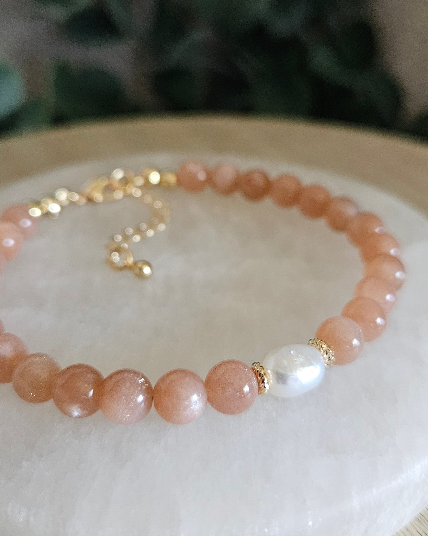 Close-up of peach Sunstone beads and a freshwater pearl focal with gold-plated floral spacers