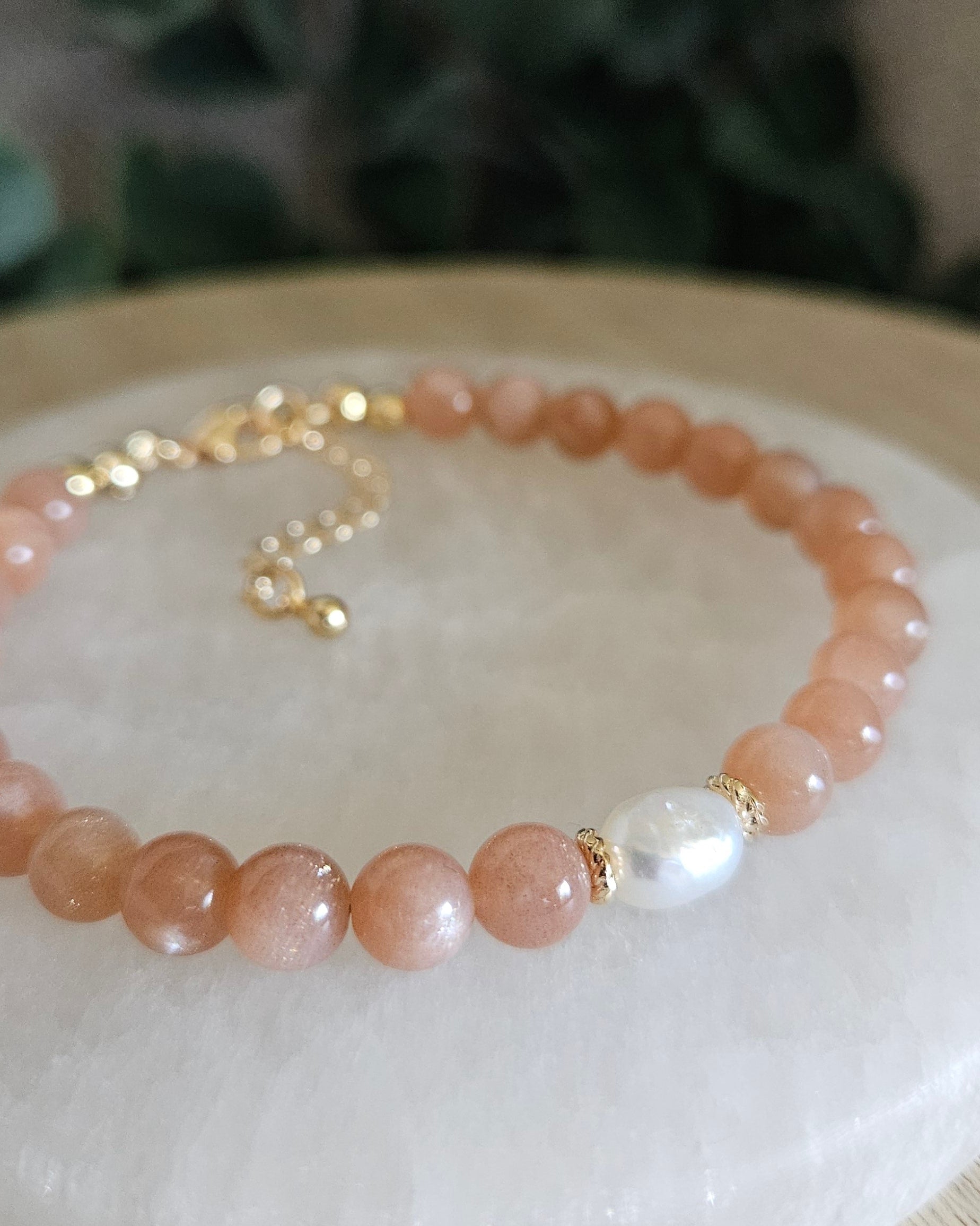 Close-up of peach Sunstone beads and a freshwater pearl focal with gold-plated floral spacers