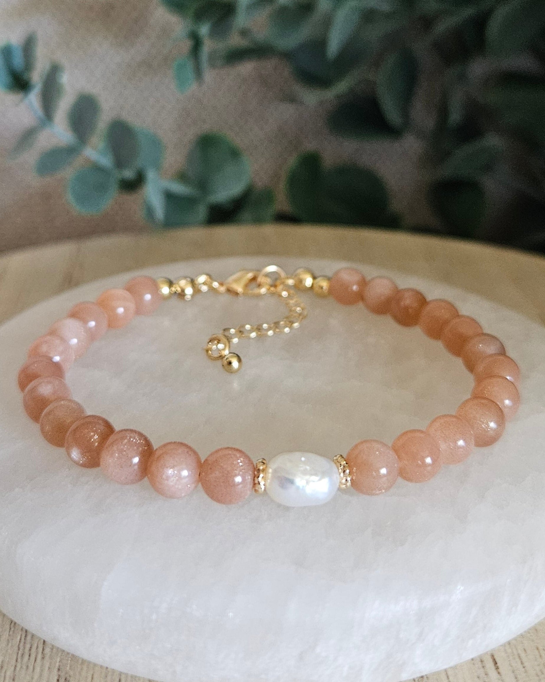 Sunstone Embrace bracelet with freshwater pearl focal and gold-plated accents displayed on a selenite plate