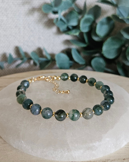Moss Agate Echo bracelet with gold-plated accents and clasp displayed on a round selenite plate