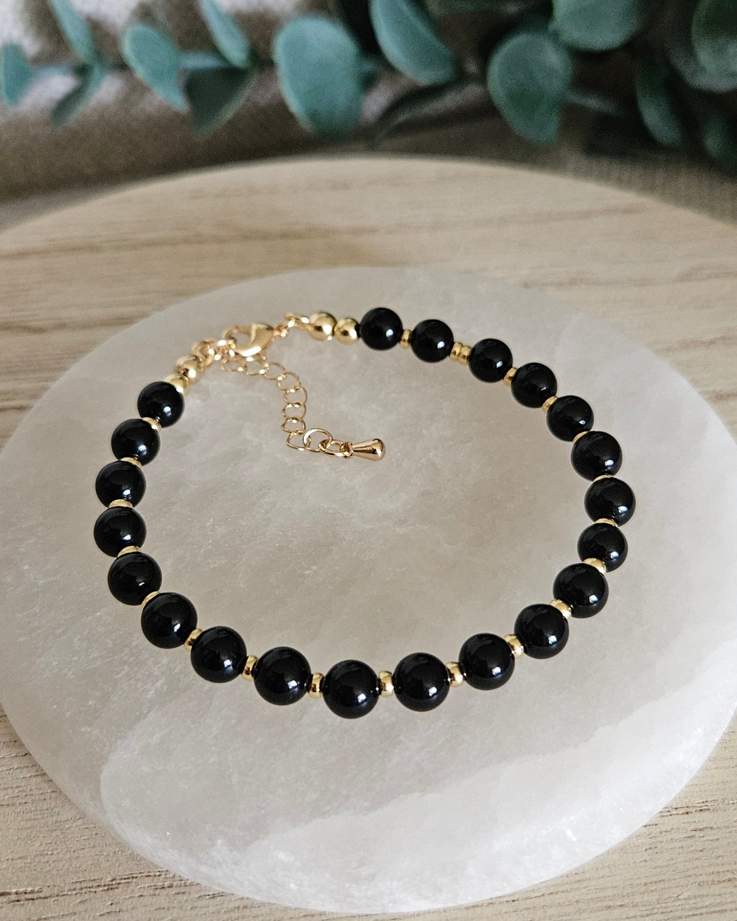 Overhead view of the Black Onyx Echo bracelet with gold-plated clasp and extender chain on selenite