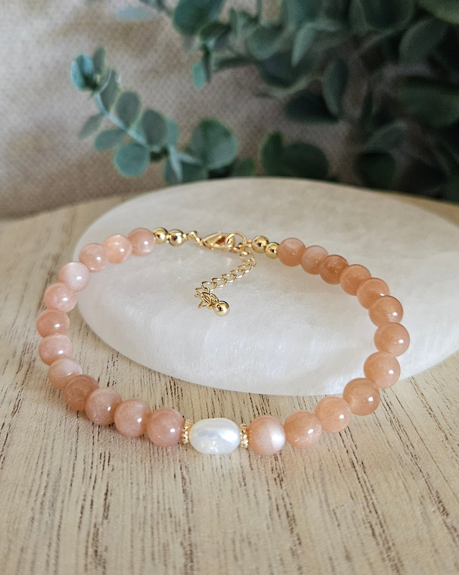 Sunstone Embrace bracelet arranged before a selenite plate with a freshwater pearl focal and eucalyptus background