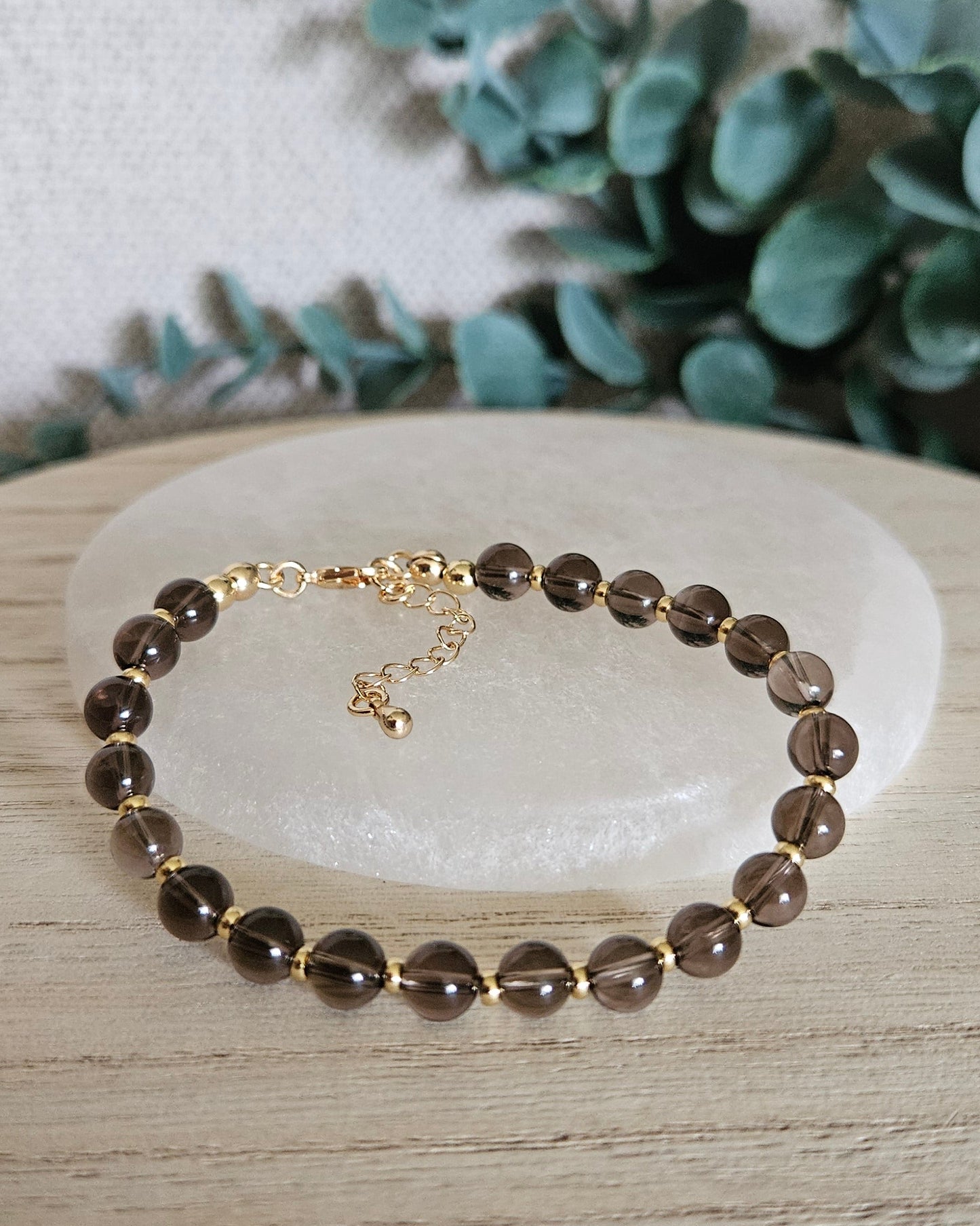 Smoky Quartz Echo bracelet arranged before a selenite plate with eucalyptus in the background