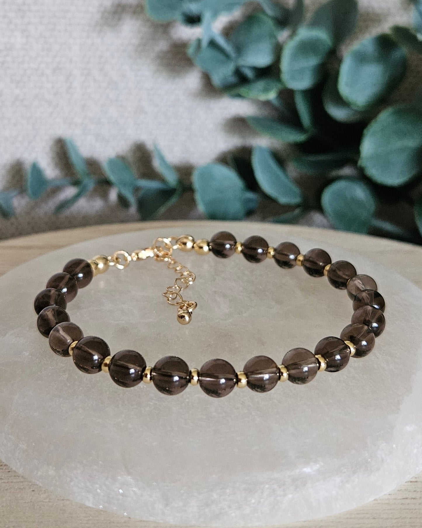 Smoky Quartz Echo bracelet with gold-plated accents and clasp displayed on a round selenite plate
