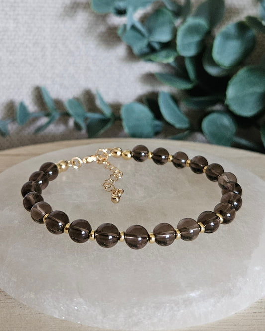 Smoky Quartz Echo bracelet with gold-plated accents and clasp displayed on a round selenite plate