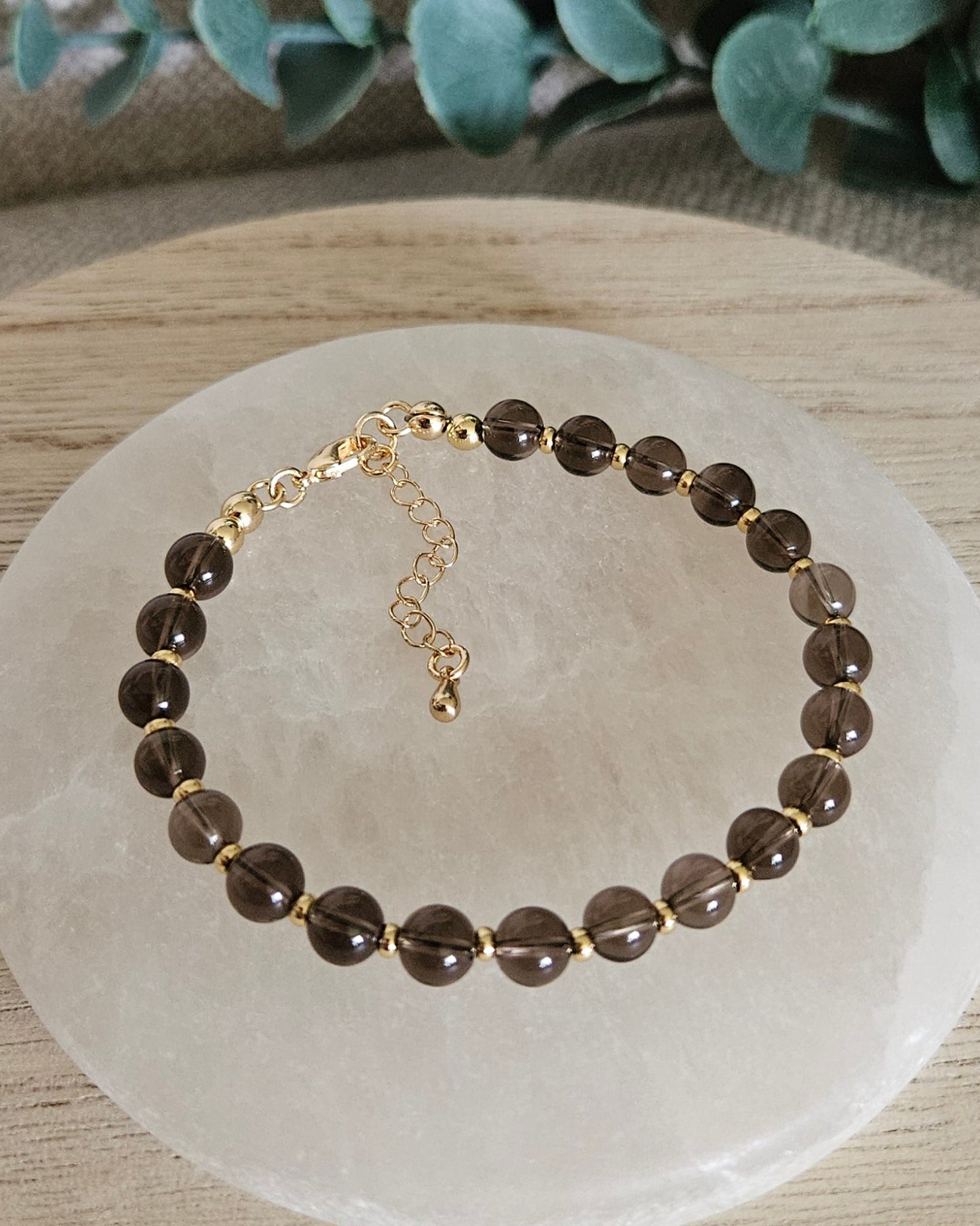 Overhead view of the Smoky Quartz Echo bracelet with gold-plated clasp and extender chain on selenite