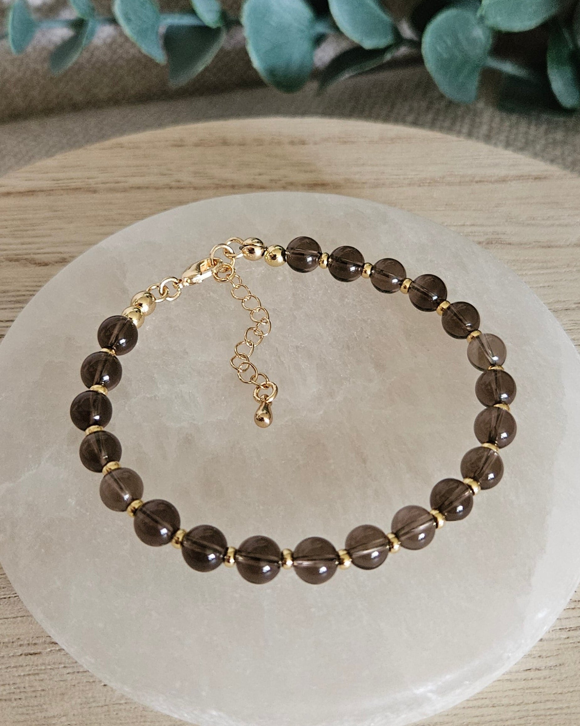 Overhead view of the Smoky Quartz Echo bracelet with gold-plated clasp and extender chain on selenite