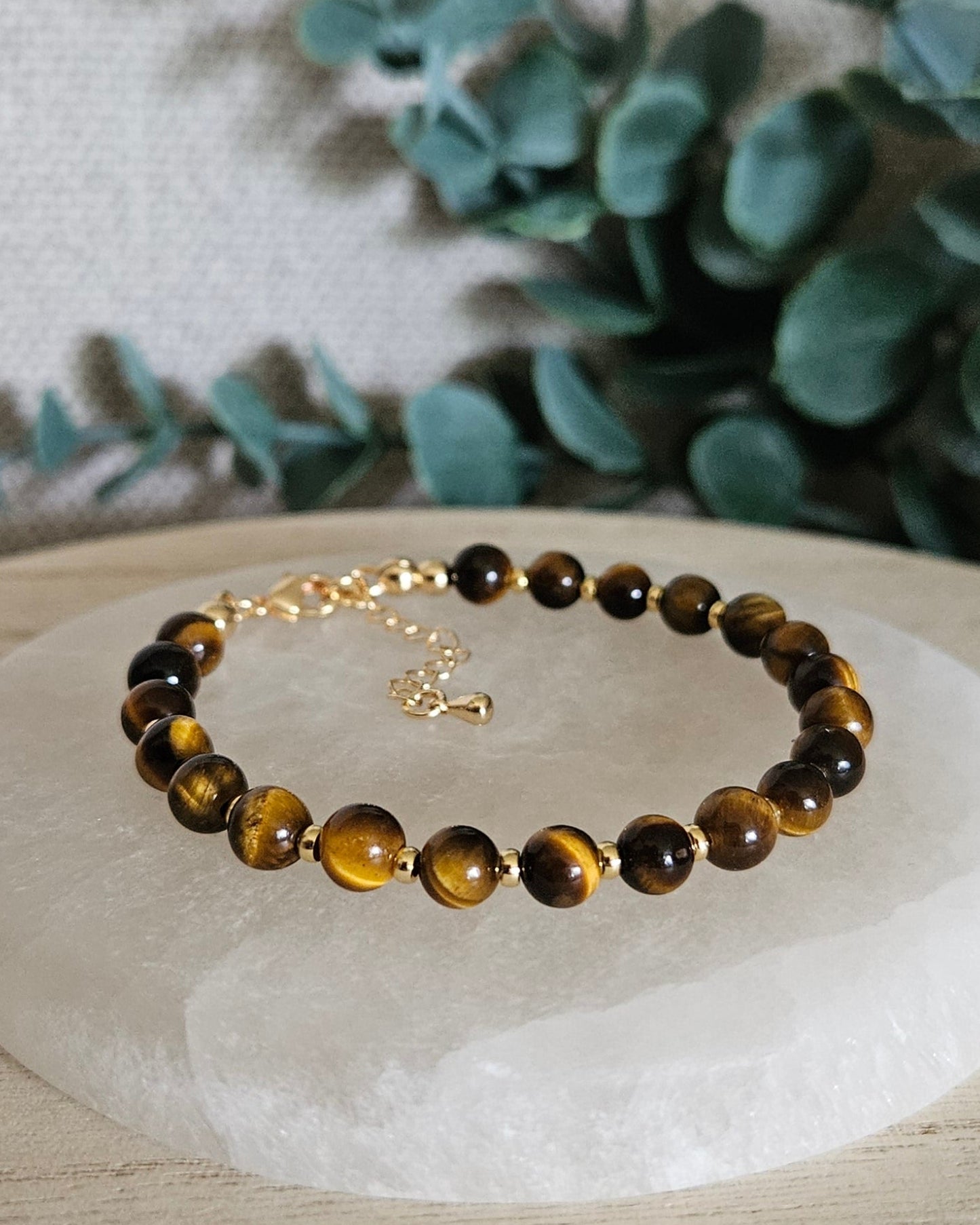 Tiger’s Eye Echo bracelet with gold-plated accents and clasp displayed on a round selenite plate