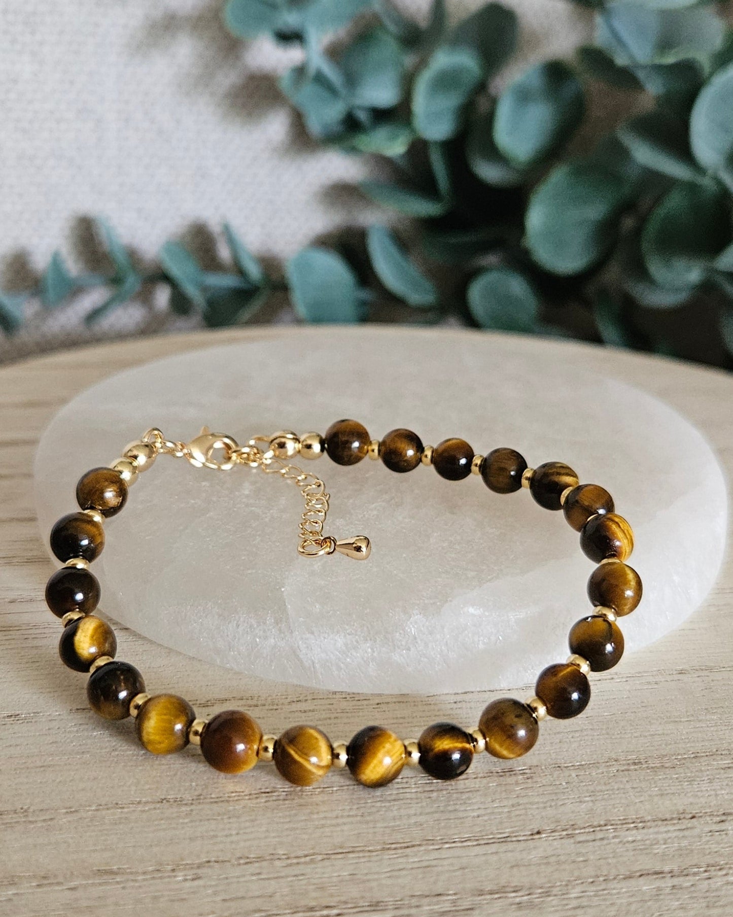 Tiger’s Eye Echo bracelet arranged before a selenite plate with eucalyptus in the background