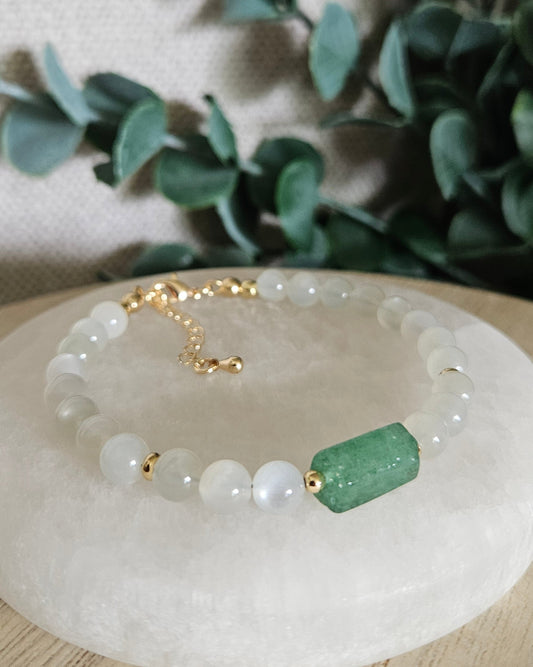 White Moonstone bracelet with a Green Strawberry Quartz barrel focal and gold accents displayed on a round selenite plate