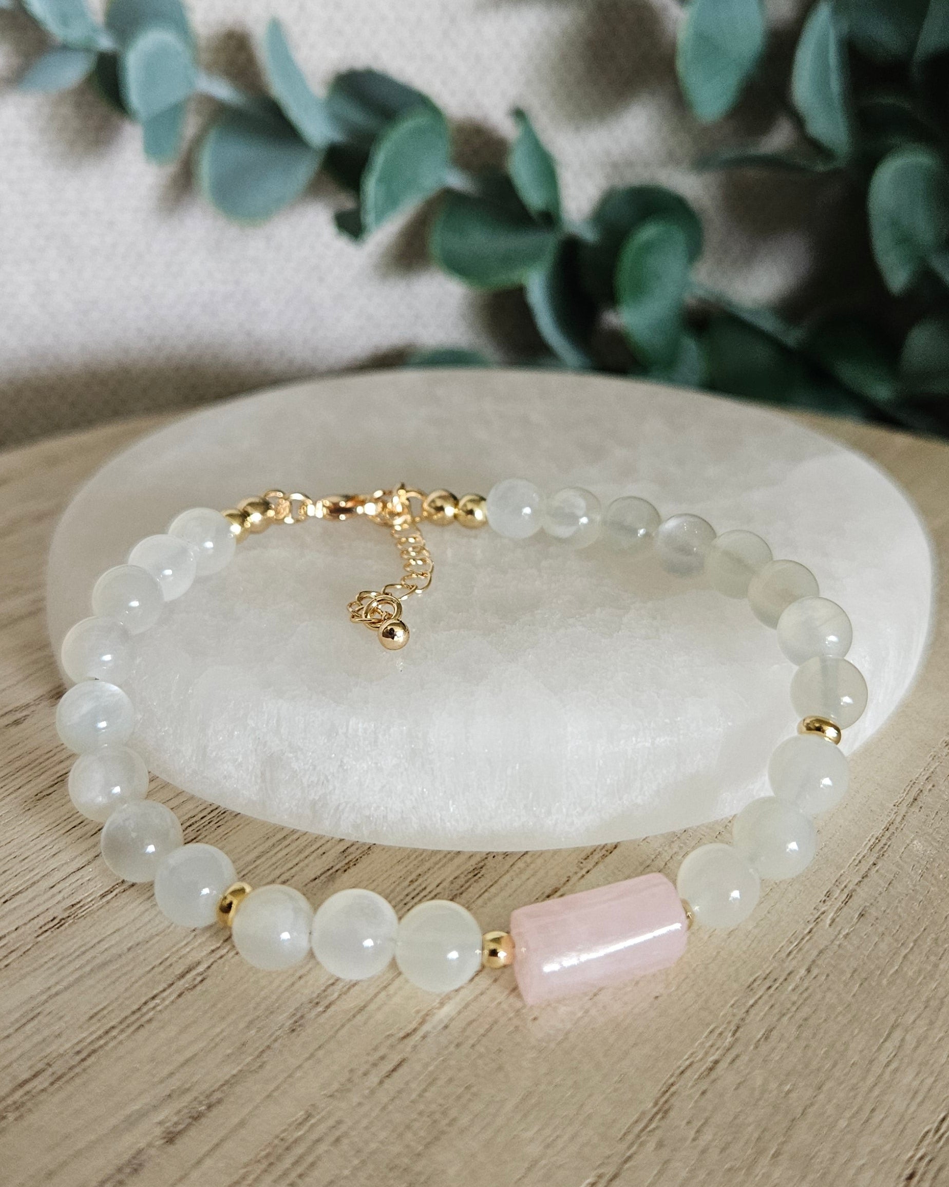 White Moonstone and Rose Quartz bracelet arranged before a selenite plate with eucalyptus in the background
