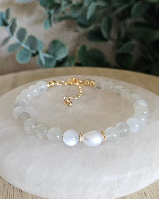 White Moonstone Embrace bracelet with freshwater pearl focal and gold-plated accents displayed on a selenite plate
